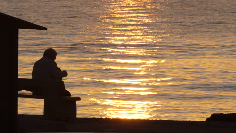 Mann-Chillt-Vor-Dem-Sonnenaufgang,-Orangefarbene-Reflexionen,-Sonne,-Mittelmeer
